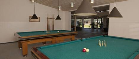 A pool table with a green felt surface, wooden table, and several pool cues. There are hanging pendant lights and a wooden ceiling.