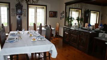 A dining room with a long table set for a meal, wooden chairs, a large clock, and a mirror reflecting the room.
