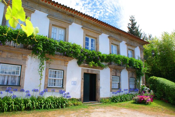 Traditional building with a central entrance and climbing plants, set amidst well-maintained gardens.