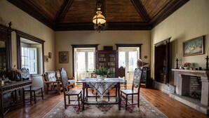 Um quarto espaçoso com piso de madeira, uma mesa de jantar com cadeiras, uma lareira e uma janela grande.