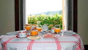 Mesa de café da manhã posta com pratos, copos e um jarro de suco de laranja, com vista para o verde lá fora.