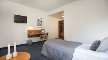 A hotel room with a bed, a desk with a chair, a TV mounted on the wall, and a coat rack.