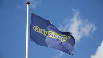 A flag with the text "OnlySleep" on a flagpole against a clear blue sky.