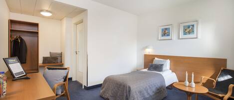 A hotel room with a bed, bedside table, chair, desk, and a wardrobe.