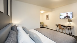 A modern hotel room with a neatly made bed, a desk with a chair, and a television on the wall.