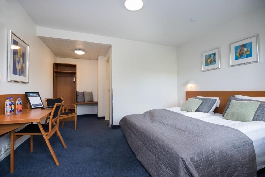 A hotel room with a bed, desk, chair, and a wardrobe.