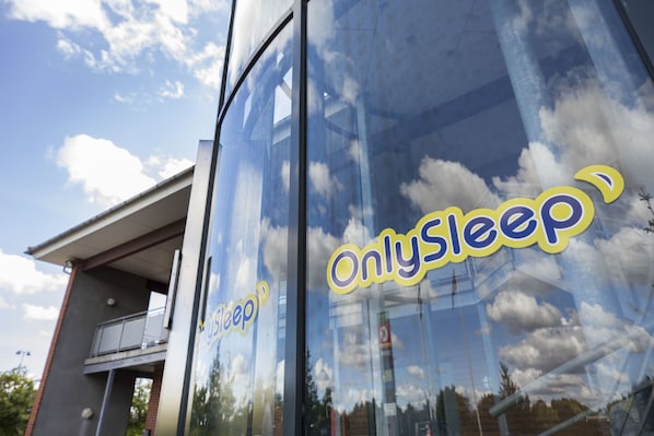 A building with a glass facade reflecting clouds and sky. The text "OnlySleep" is visible on the glass.