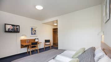 A hotel room with a bed, a desk, a chair, a TV, and a wardrobe.