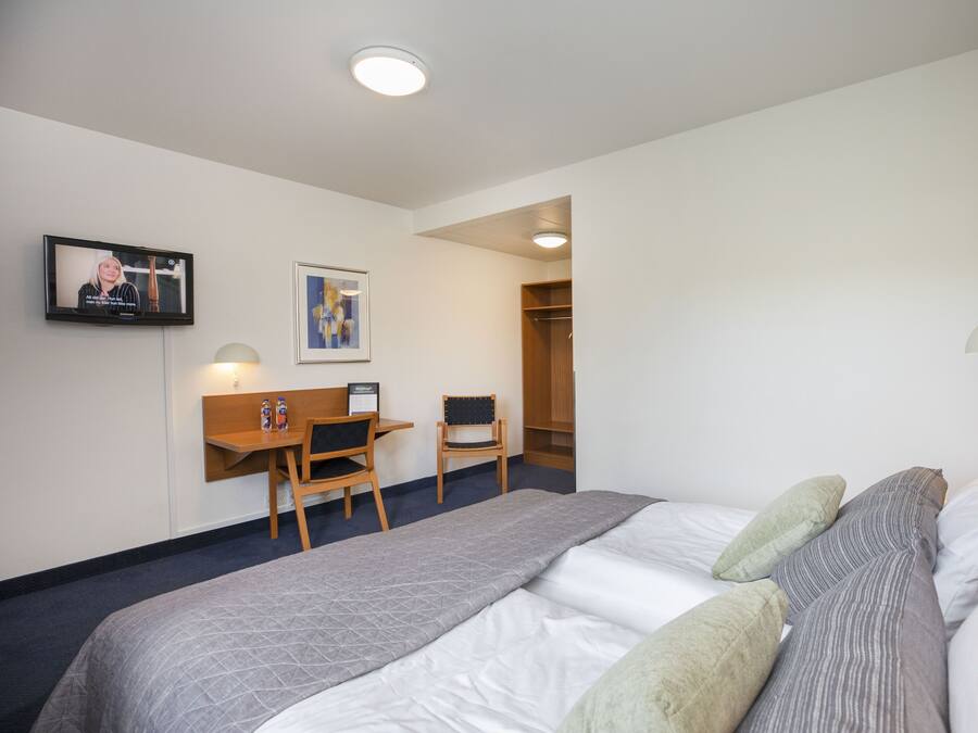 Une chambre d’hôtel équipée d’un lit, d’un bureau, d’une chaise, d’une télévision et d’une armoire.