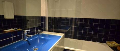 Une salle de bain avec un lavabo bleu, une baignoire blanche et une cabine de douche en verre.