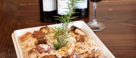 Un plato blanco cuadrado con arroz y carne, acompañado de tres botellas de vino y una copa de vino tinto sobre una mesa de madera.