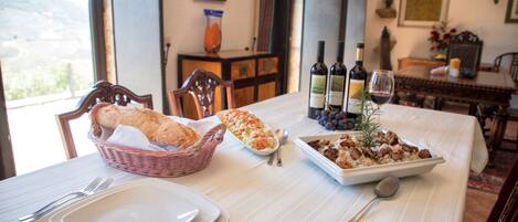 A dining table set with plates, a basket of bread, a dish of food, and wine bottles.