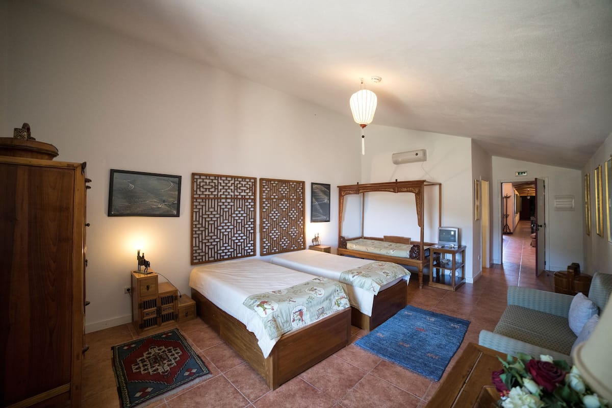 A bedroom with two wooden beds, a wooden wardrobe, a small bedside table, a wall-mounted TV, and a decorative wall panel.