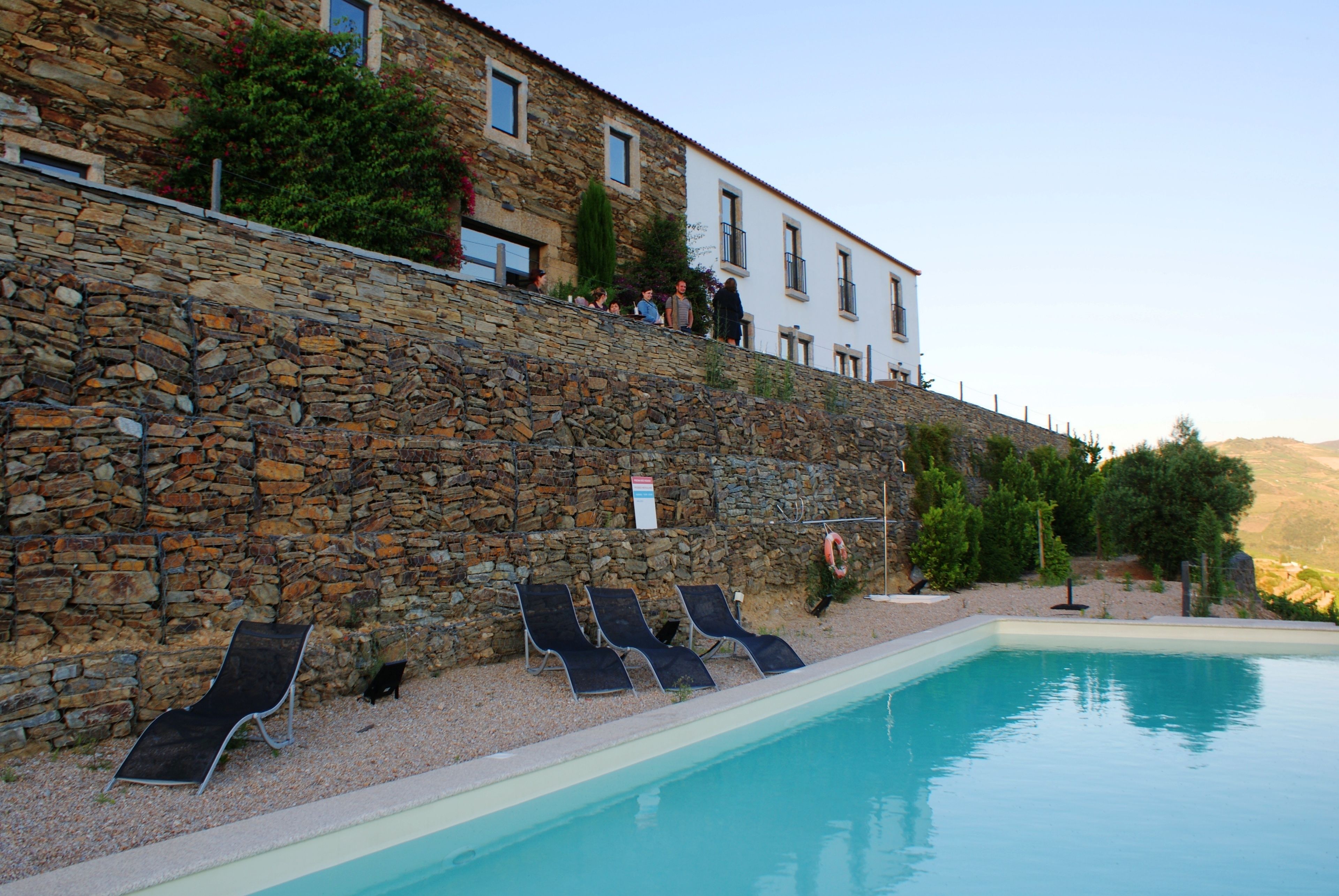 A stone wall with a pool and lounge chairs.