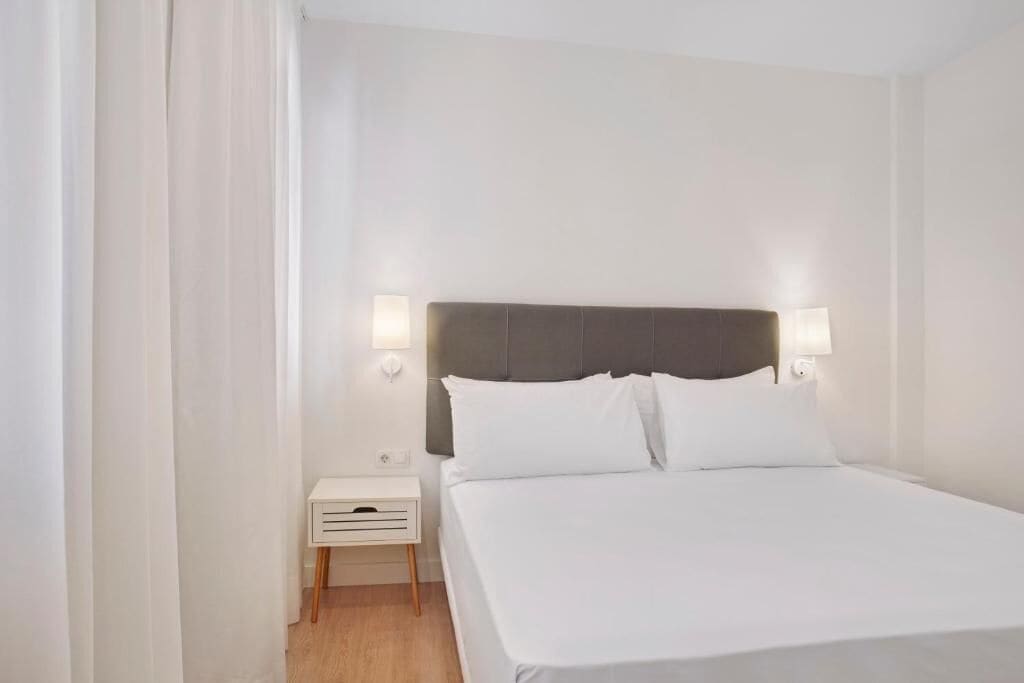 Una habitació d'hotel amb un llit, una tauleta de nit i dues làmpades penjades a la paret.