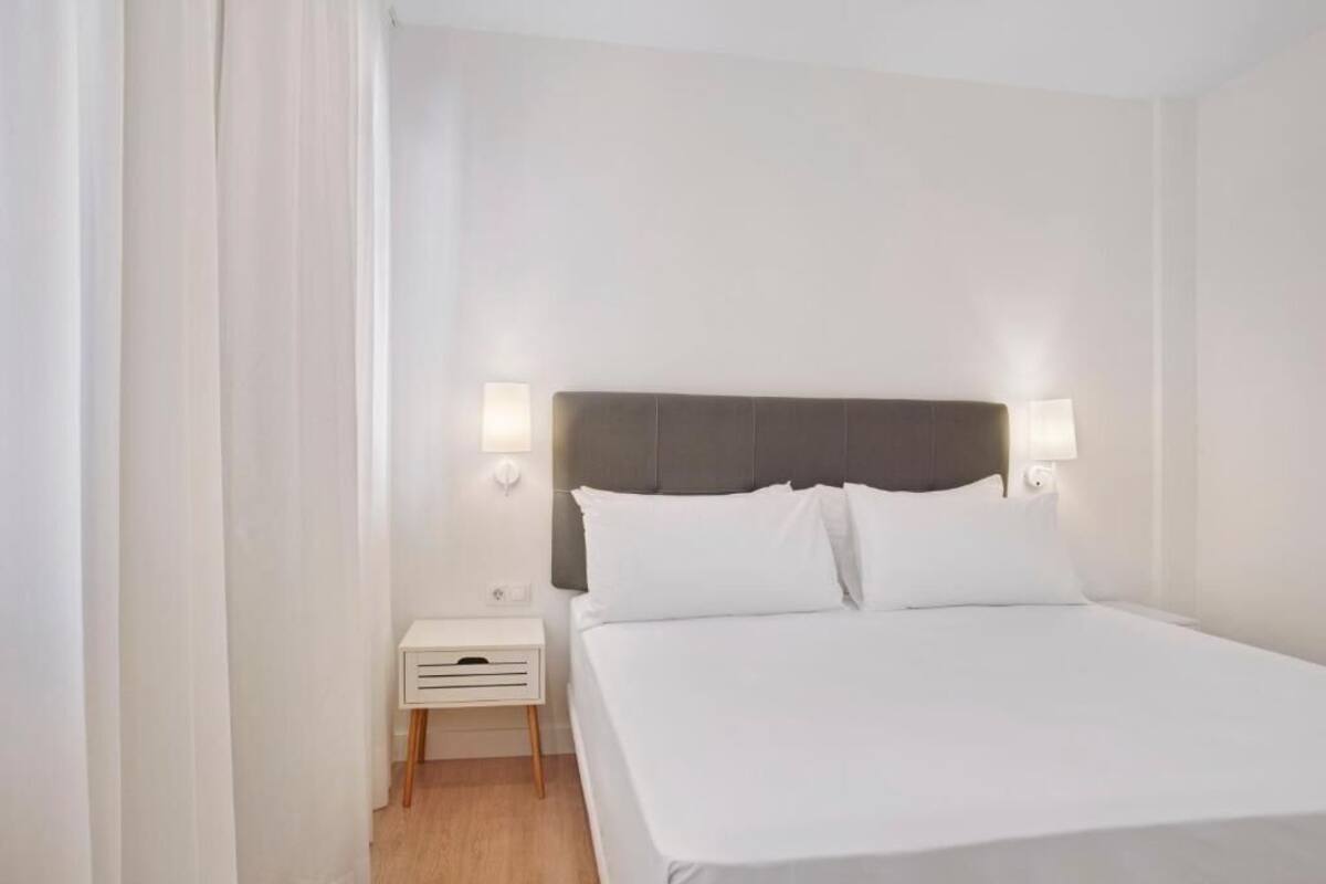 Una habitación de hotel con una cama, una mesita de noche y dos lámparas de pared.