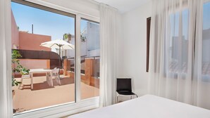 Habitación de hotel con un amplio ventanal corredera que da a un patio al aire libre, una cama, una silla y una mesa.