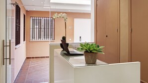 Un área de recepción moderna con un escritorio de vidrio, una computadora portátil, una planta en maceta y un ventanal con vistas al exterior.
