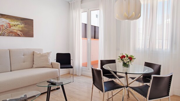 Una sala moderna con sofá, una mesa de centro de vidrio, una mesa de comedor con sillas y un cuadro en la pared.