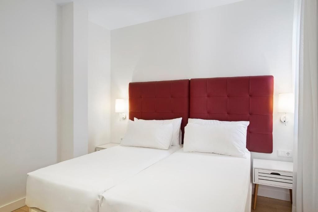 Un lit double avec une tête de lit rouge, une literie blanche et deux tables de chevet avec des lampes.