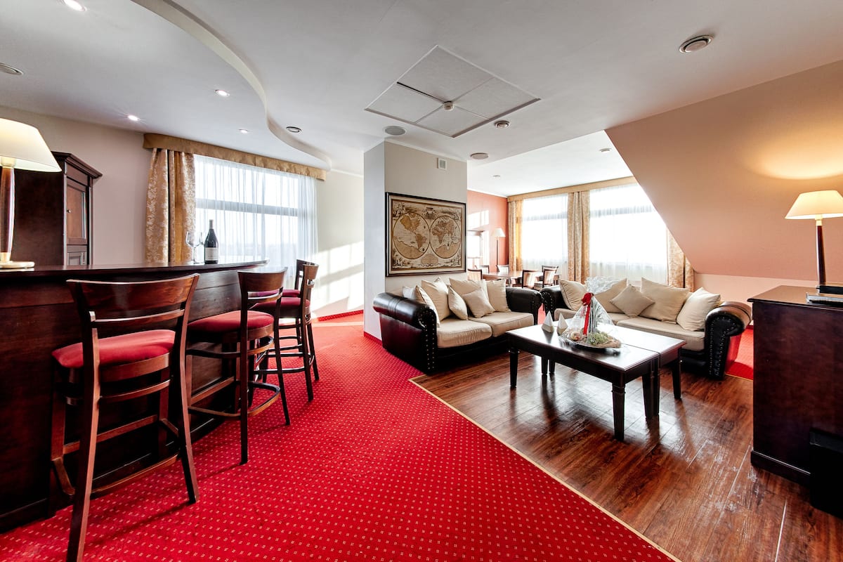 A hotel room with a red carpet, a sofa set, a dining table, and a bar area.