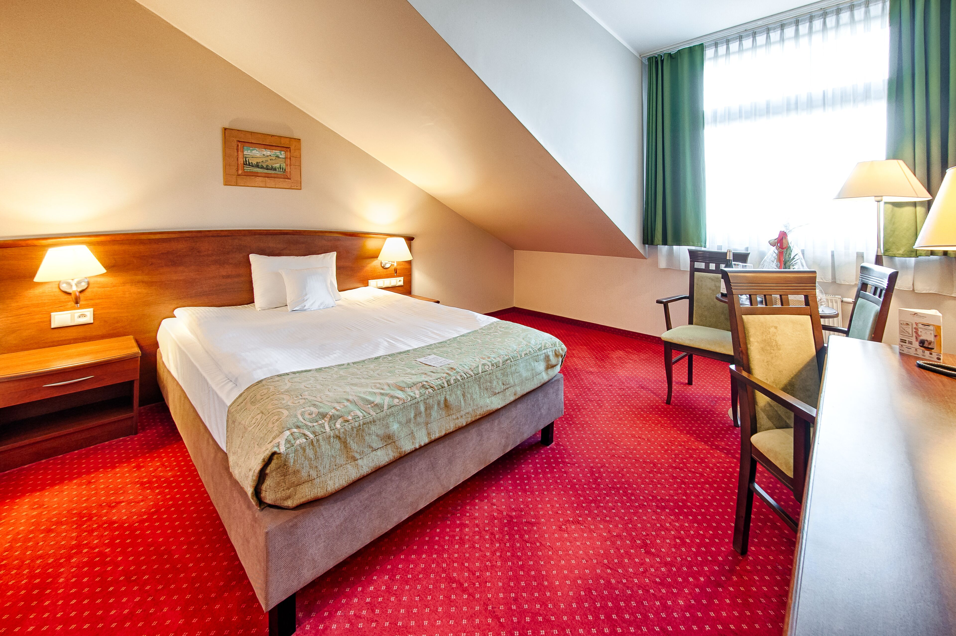 Habitación de hotel con cama, dos lámparas de noche, escritorio con silla y ventana con cortinas.