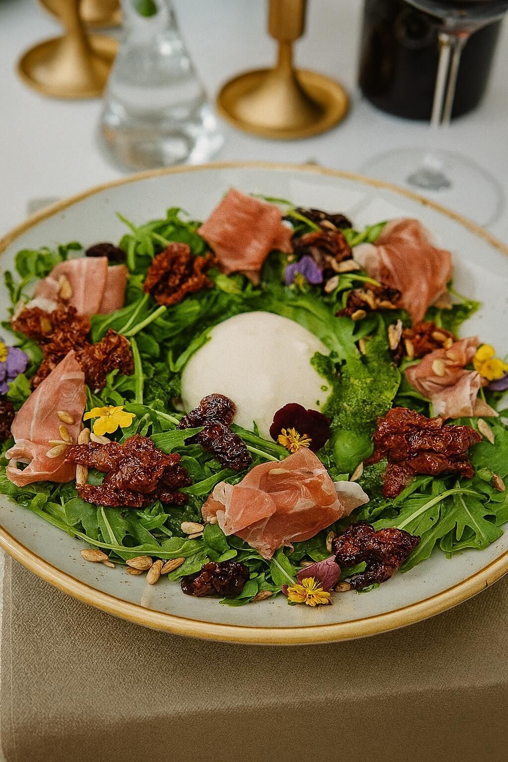 A plate of salad with greens, nuts, and prosciutto.