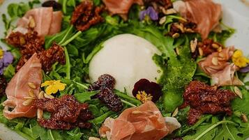 A plate of salad with greens, nuts, and prosciutto.
