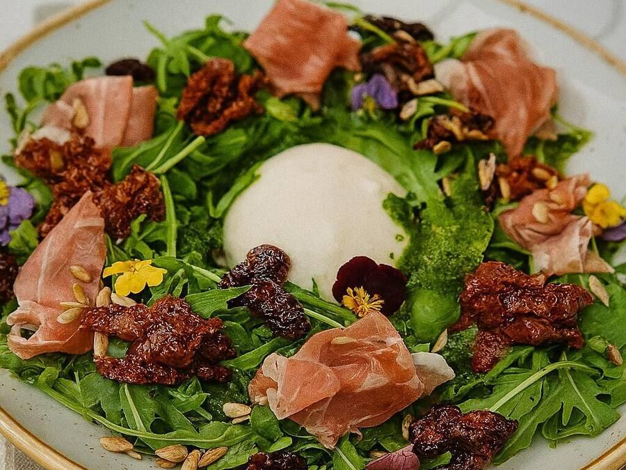 A plate of salad with greens, nuts, and prosciutto.
