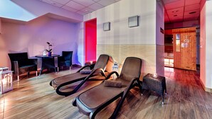 Un espace de détente moderne comprenant des fauteuils inclinables, une petite table avec une bougie et un fauteuil de massage fixé au mur.