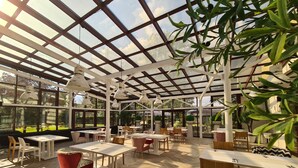 Un jardin intérieur avec des tables et des chaises, de grandes fenêtres et des plantes suspendues.