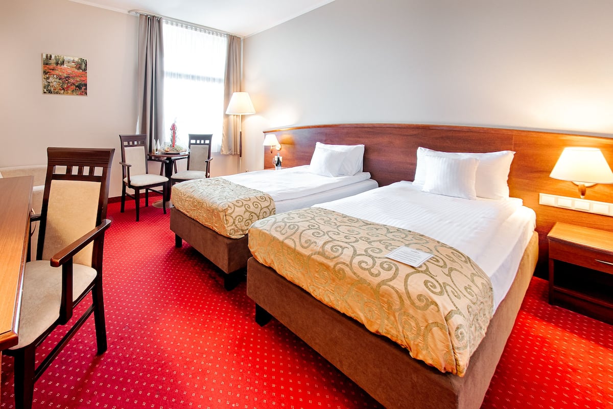 A hotel room with two beds, a desk, chairs, and a window with curtains.