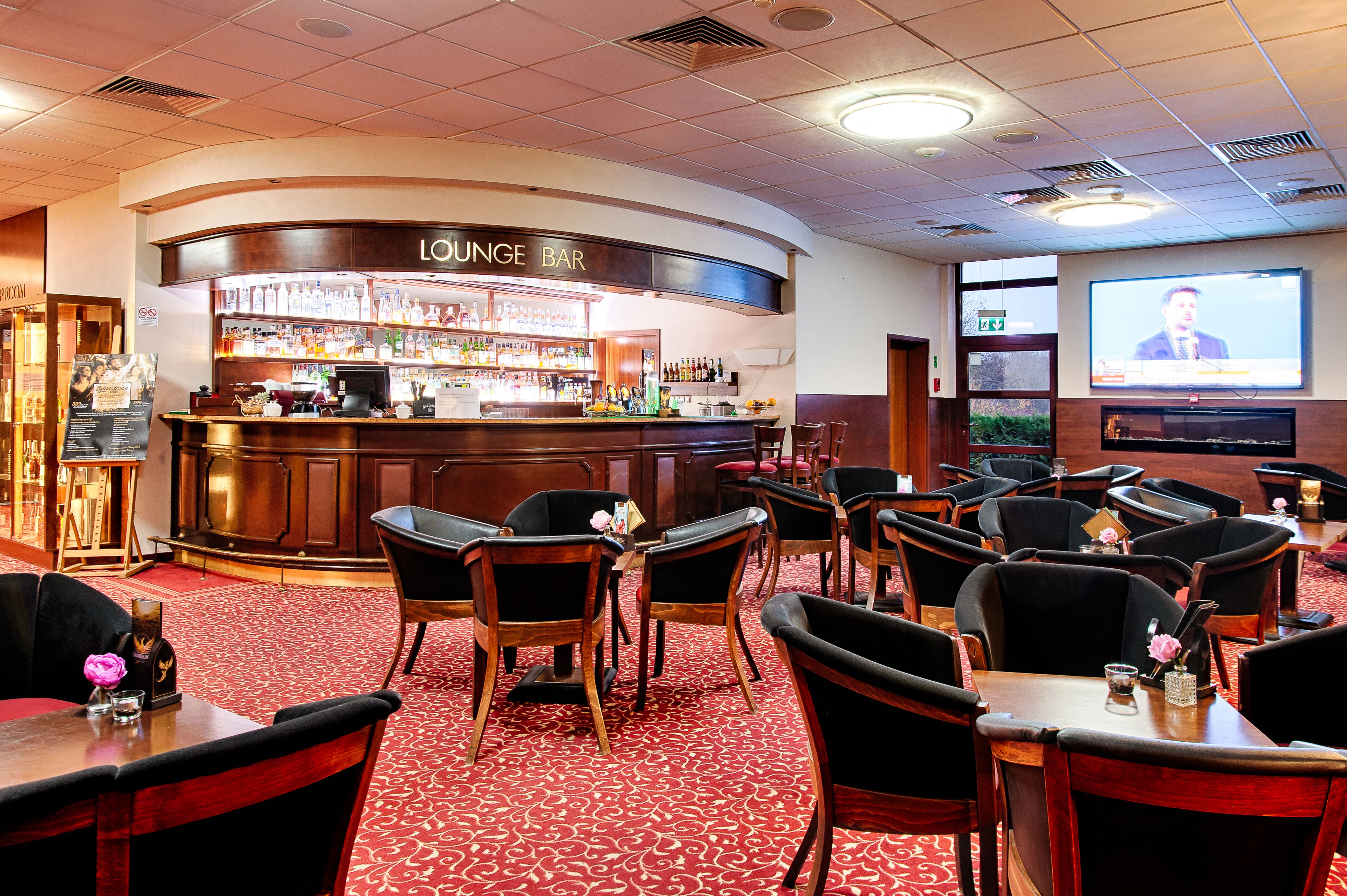 Eine Lounge-Bar mit Barbereich, mehreren Sitzbereichen und einem großen Bildschirm, der eine Präsentation zeigt.