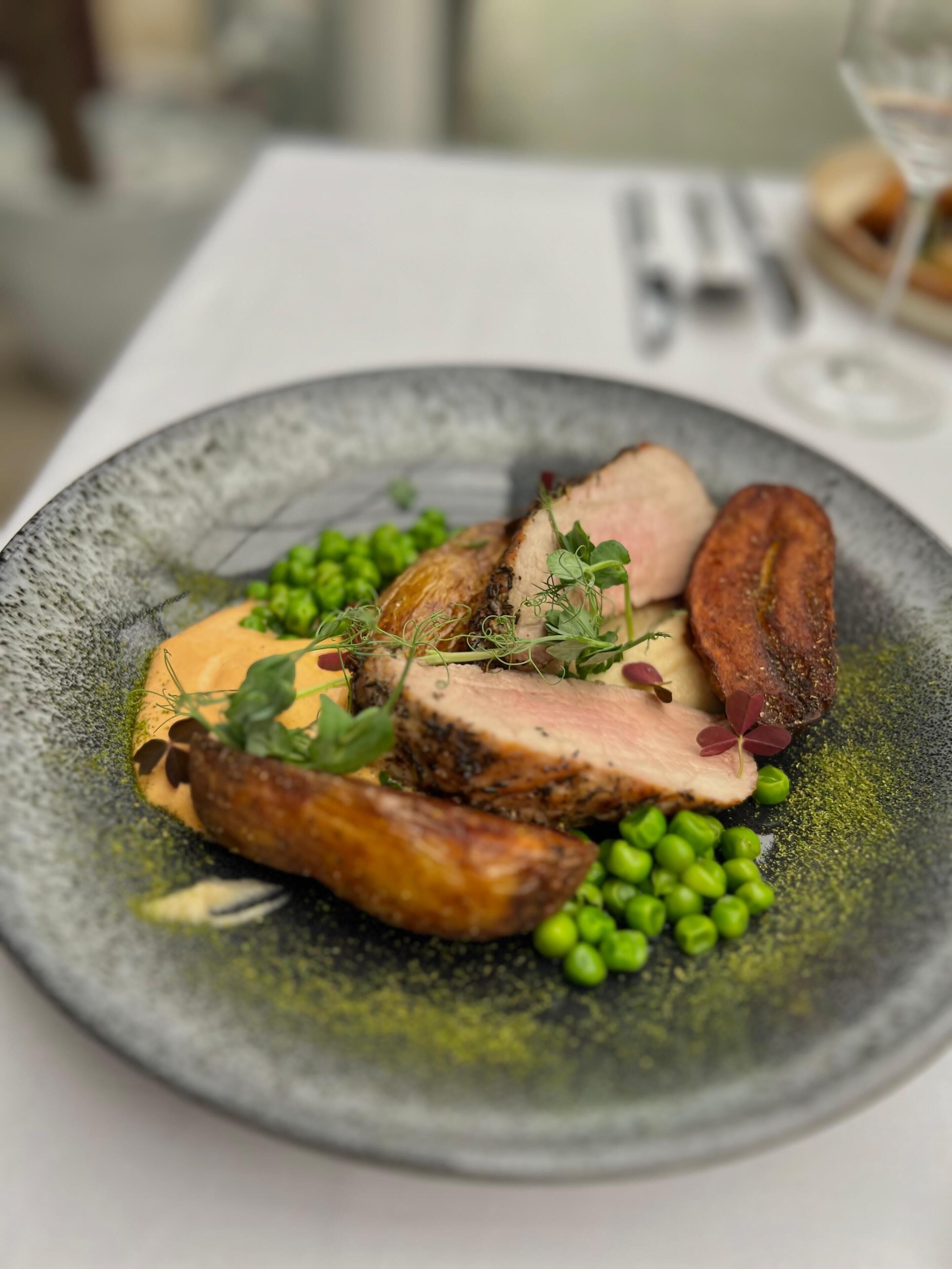 A plate of food with sliced meat, peas, and a sauce.