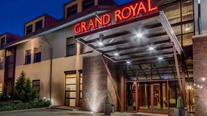 L’entrée d’un hôtel, avec une enseigne bien visible indiquant « GRAND ROYAL », de grandes portes vitrées et un espace d’entrée abrité.