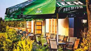 Un espace extérieur aménagé avec des tables et des chaises, protégé par des parasols verts sur lesquels est inscrit « LECH PREMIUM ».