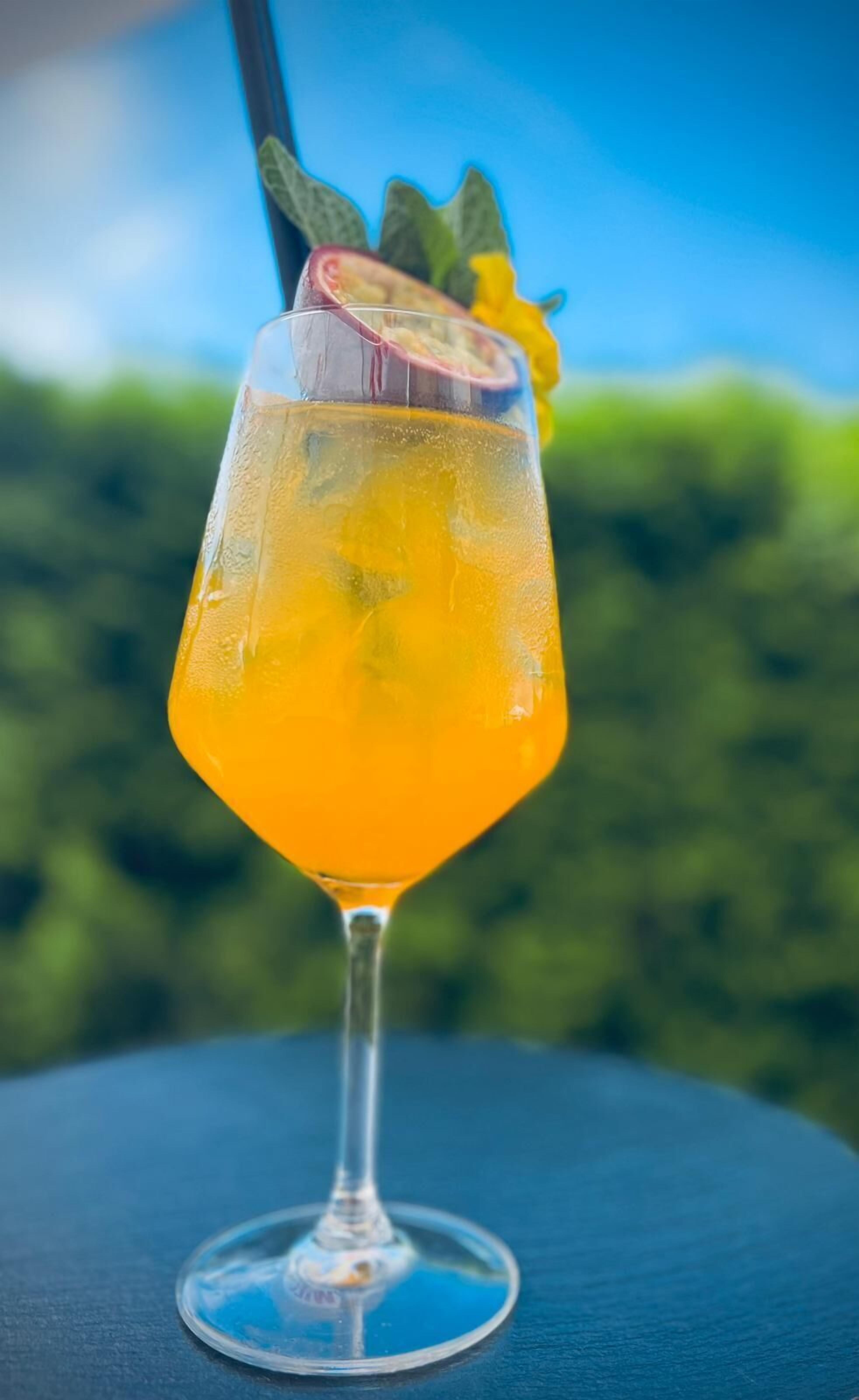 Ein Cocktailglas mit einem gelben Getränk, einem Strohhalm und einer Minzdekoration auf einem Tisch mit blauer Oberfläche.