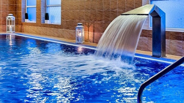 Une piscine agrémentée d’un élément aquatique, dotée de murs carrelés et de lanternes décoratives.