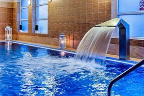 A swimming pool with a water feature, tiled walls, and decorative lanterns.