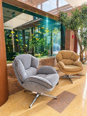 A modern interior with two upholstered chairs, a glass aquarium with yellow fish, and a potted plant. - Grand Royal Hotel (Poznan)
