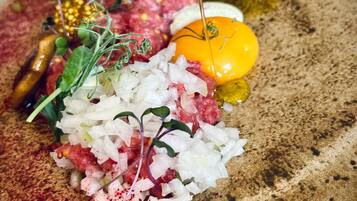 Ein Detailbild von einem Teller mit rohem Fleisch, Gemüse und einem gelben Eigelb, das mit Öl beträufelt wird.