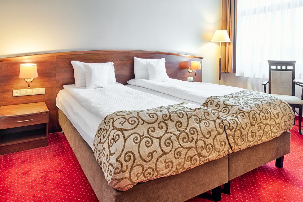 A hotel room with a double bed, two bedside tables, a chair, and two wall-mounted lamps.