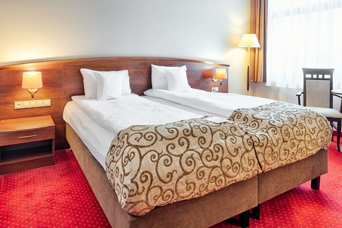 A hotel room with a double bed, two bedside tables, a chair, and two wall-mounted lamps.