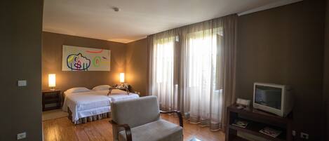 A hotel room with two beds, a sofa, a TV, and a painting on the wall.