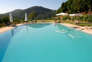 A clear blue pool with lounge chairs and umbrellas, surrounded by greenery and hills. - Casa do Condado de Beirós (Sao Pedro do Sul)