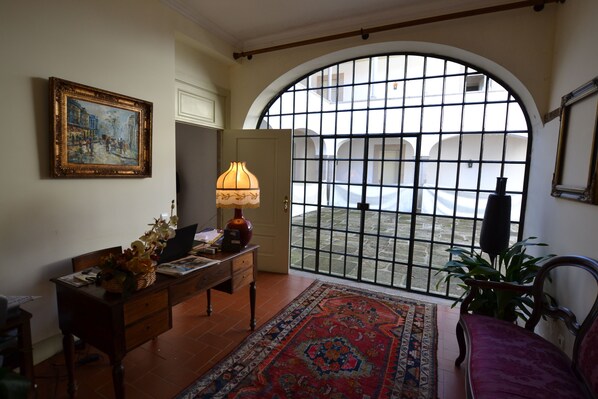 A room with a desk, chair, lamp, and a large arched window with a view of a courtyard. - Casa do Condado de Beirós (Sao Pedro do Sul)