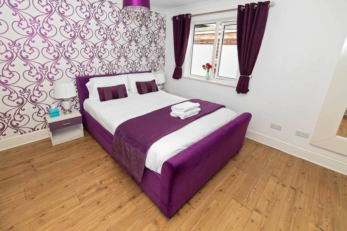 A bedroom with a purple bed, white walls, and a patterned wallpaper.