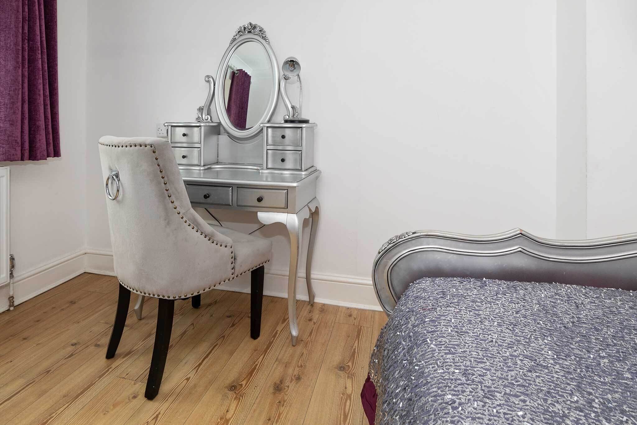 Un dormitorio con tocador, cama y ventana con cortinas.