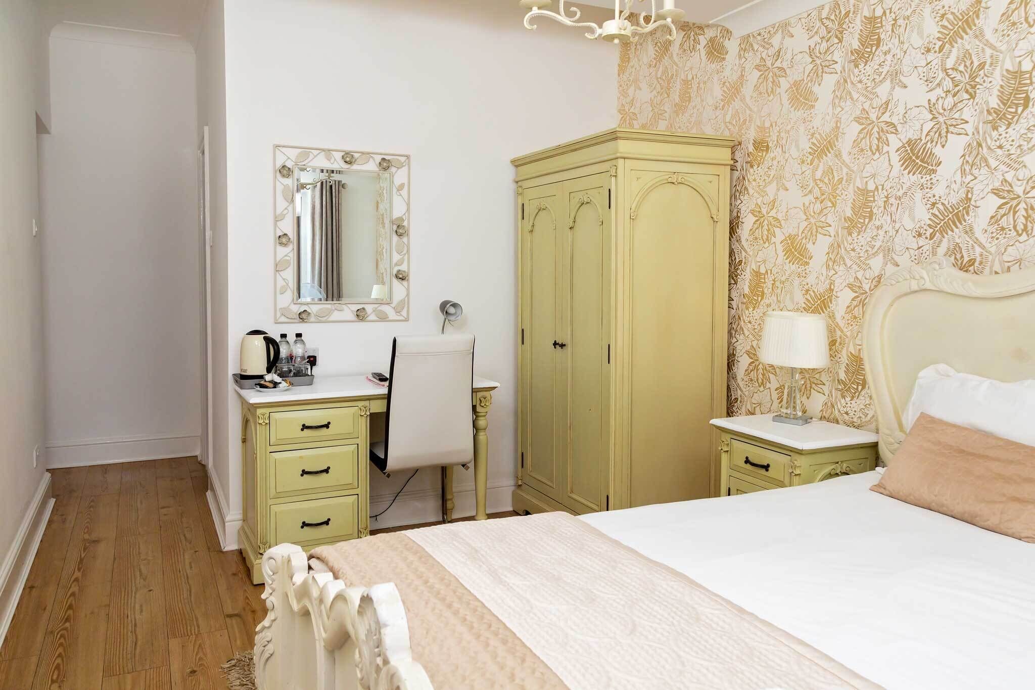 A bedroom with a bed, a dresser with drawers, a mirror, a wardrobe, and a desk with a chair.
