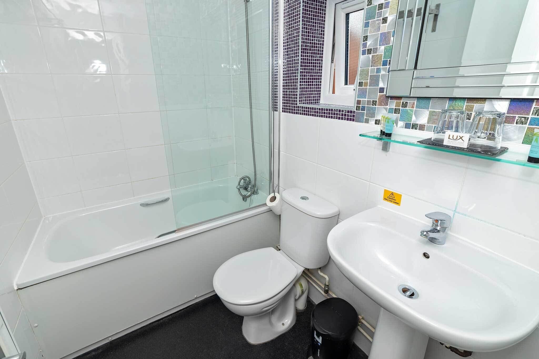 Un baño con ducha envuelta en vidrio, inodoro y lavamanos blancos, y un salpicadero de azulejos.